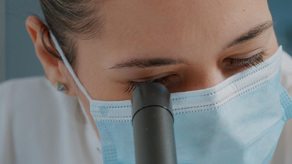 Woman scientist using microscope with magnifying glass for science experiment in laboratory. Specialist wearing face mask, working with microscopic lens on scientific tool. Close up